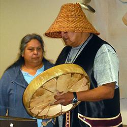 His wife Annette beside him, Merlin Bullchild performs a traditional welcoming song.